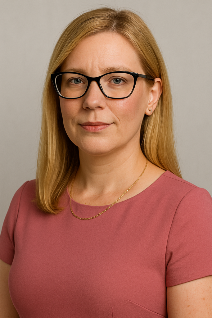 Woman with long blonde hair and glasses, wearing a pink dress, poses against a neutral background.